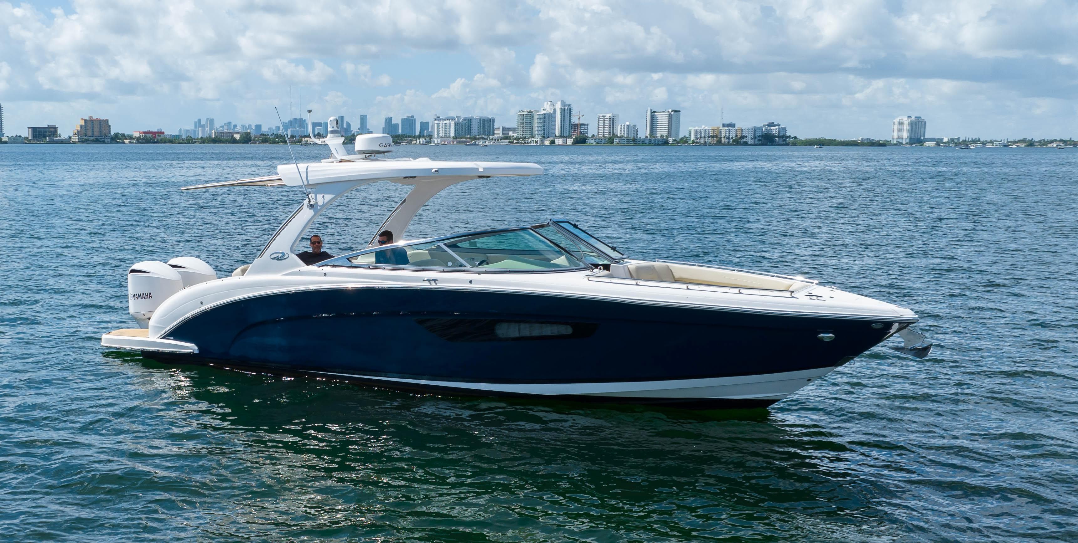 2019 Regal 33 OBX boat cruising on a calm sea with city skyline in background.