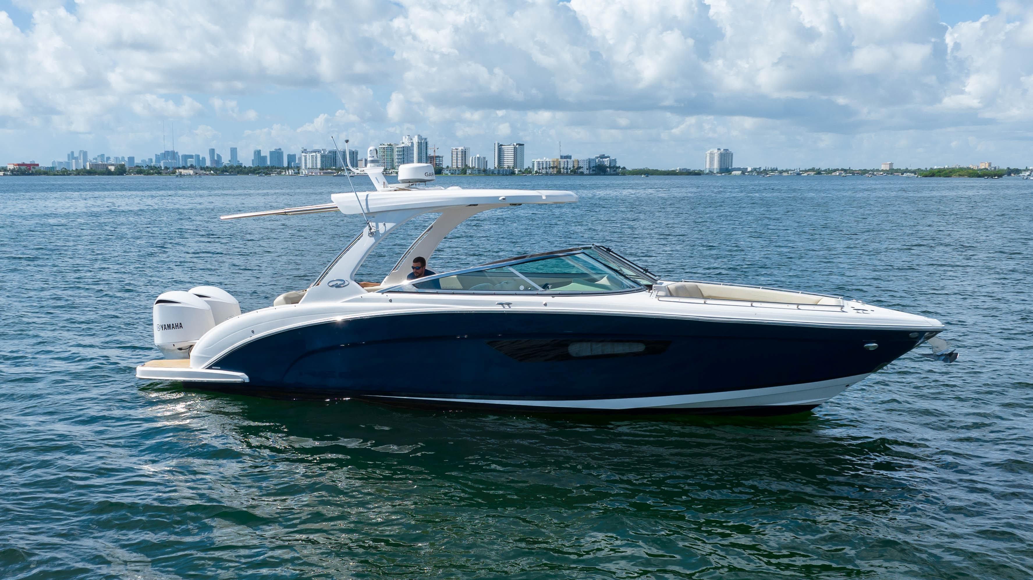 2019 Regal 33 OBX boat cruising on a sunny day with city skyline in background.